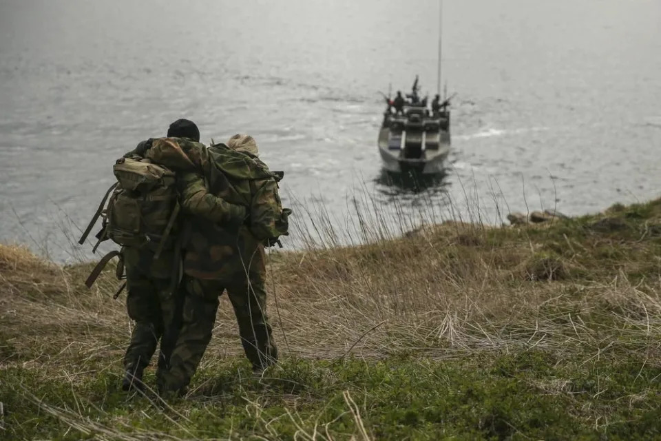 A commando propping up another person as they walk to a CB90-class fast assault craft.