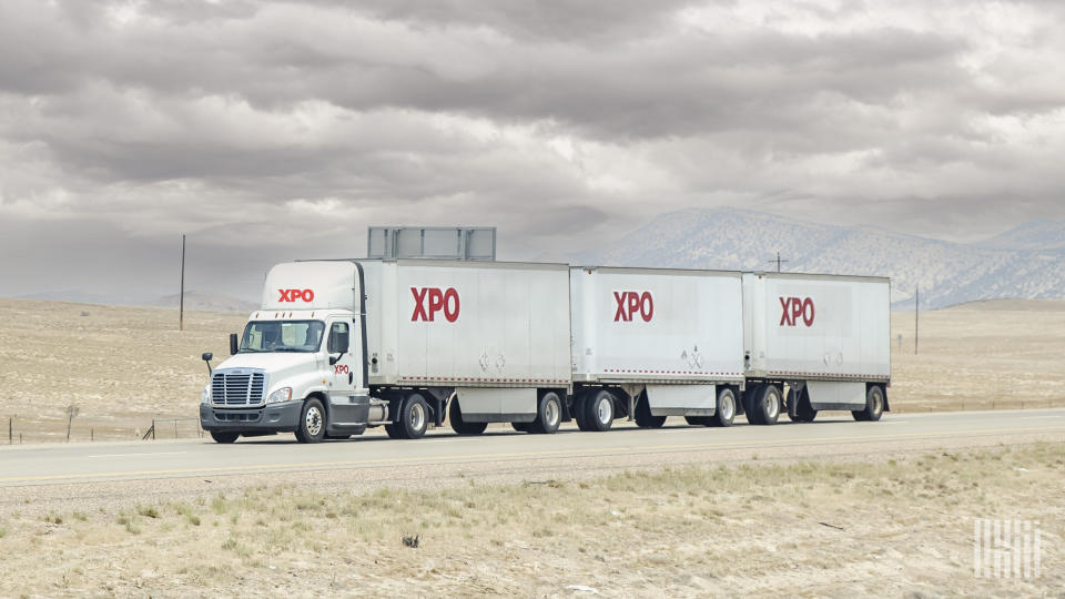 An XPO tractor pulling three XPO trailers on the highway
