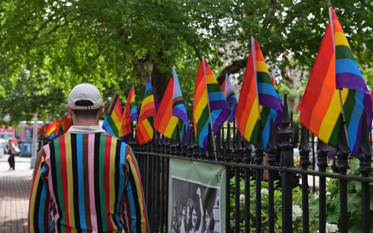 A person wearing a sweater with 'Progress Pride Flag' colors, including rainbow and black and brown stripes for communities of color, walks past rainbow flags at the Stonewall National Monument, the first US national monument dedicated to LGBTQ history and rights, marking the birthplace of the modern lesbian, gay, bisexual, transgender, and queer civil rights movement, on June 1, 2020 in New York City.  - AFP via Getty Images