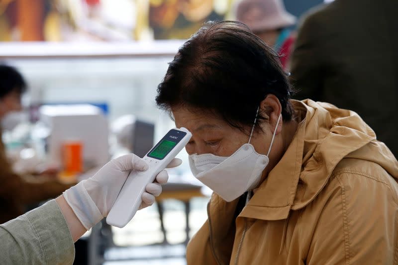 A woman wearing a preventive face mask has her temperature checked at a polling station in Seoul