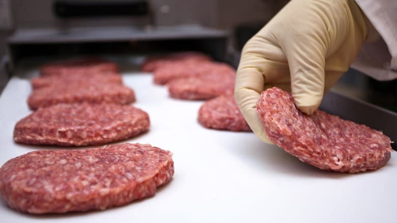 A gloved hand setting raw beef patties on a tray