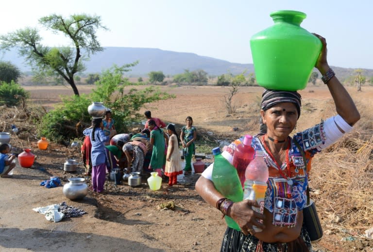 An Indian Lambadi tribal villager carries water containers as others fill drinking water from a leaking pipe on a roadside at Chandampet Mandal in Nalgonda east of Hyderabad on April 25, 2016