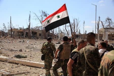 Forces loyal to Syria's President Bashar al-Assad walk at a military complex as one of them holds up a Syrian national flag, after they recaptured areas in southwestern Aleppo on Sunday that rebels had seized last month, Syria, in this handout picture provided by SANA on September 5, 2016. SANA/Handout via REUTERS/File Photo