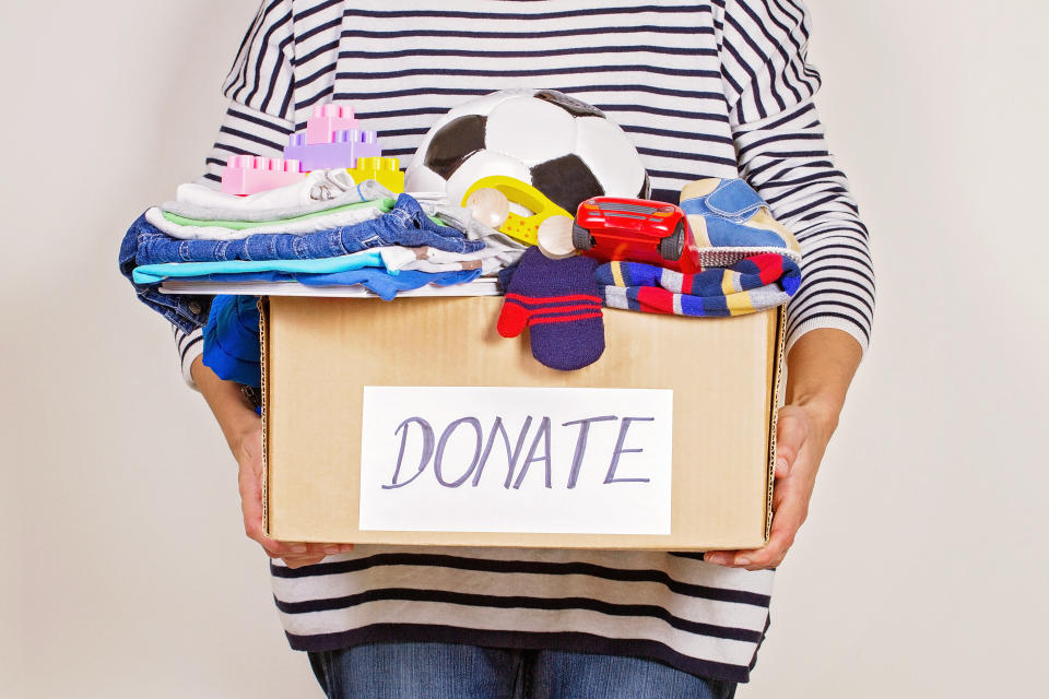 Woman hand holding donation box with clothes, toys and books. (Getty Images)