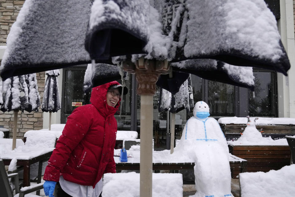 A worker at a restaurant reacts after completing a snowman in the shape of a pandemic first responder with protective suit and mask in Beijing, China, Sunday, Nov. 7, 2021. An early-season snowstorm has blanketed much of northern China including the capital Beijing, prompting road closures and flight cancellations. (AP Photo/Ng Han Guan)