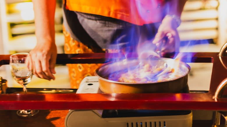 Person cooking bananas foster flambé in a pot on a stove