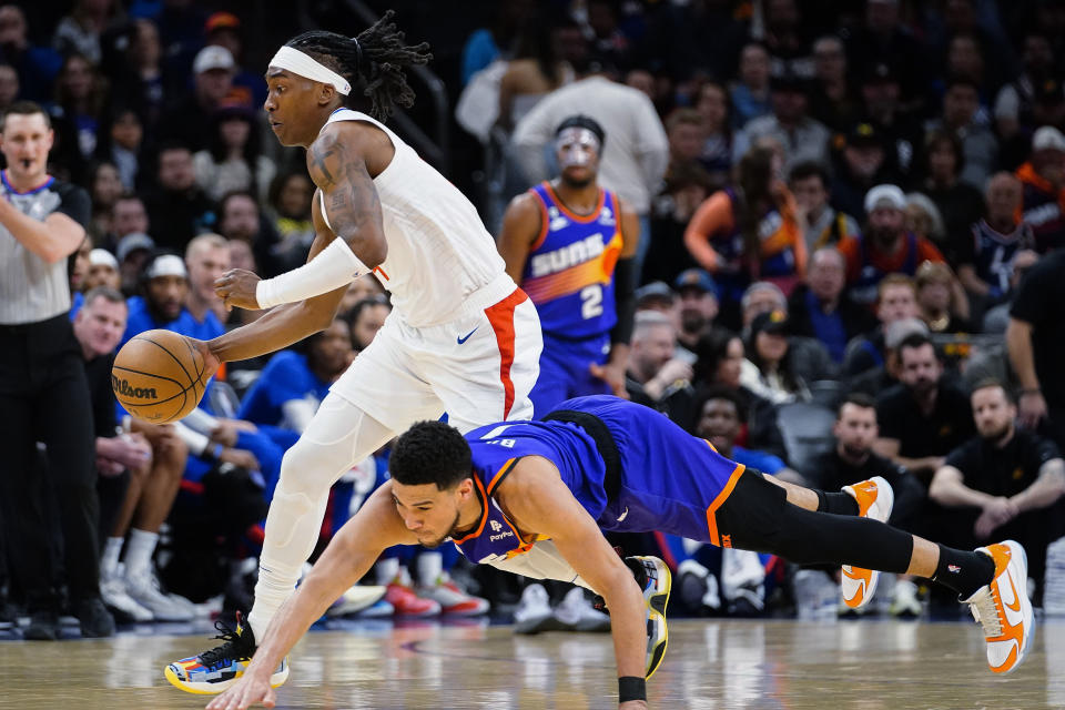 Los Angeles Clippers' Terance Mann (14) controls the ball next to a diving Phoenix Suns' Devin Booker (1) during the first half of an NBA basketball game Thursday, Feb. 16, 2023, in Phoenix. (AP Photo/Darryl Webb)
