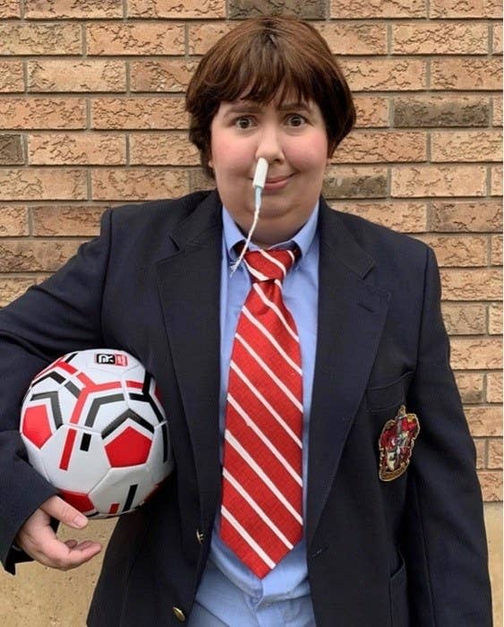 Someone in a suit, holding a soccer ball, with a tampon up their nose