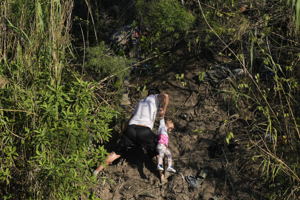 A Venezuelan migrant holds a child up as he climbs a river bank onto U.S territory, after crossing the Rio Grande river from Matamoros, Mexico, Thursday, Dec. 22, 2022. Migrants are waiting on a pending U.S. Supreme Court decision on asylum restrictions. (AP Photo/Fernando Llano)