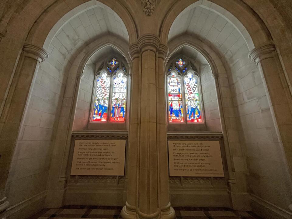 A pair of stained glass lancet windows features images of peaceful protest. Below them is a poem on the wall.