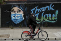 A man wearing a face mask cycles past a recently painted piece of street art by The Artful Dodger (A. Dee) entitled 'NHS Dedication Mural', thanking national health service workers, during the coronavirus lockdown in the Elephant and Castle area of London, Sunday, May 3, 2020. The highly contagious COVID-19 coronavirus has impacted on nations around the globe, many imposing self isolation and exercising social distancing when people move from their homes. (AP Photo/Matt Dunham)