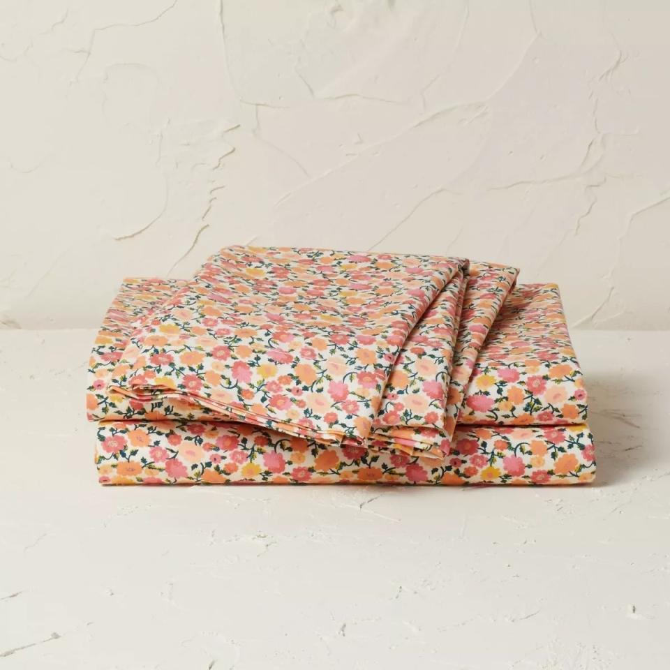 Folded floral pattern bed sheets are neatly stacked on a textured surface