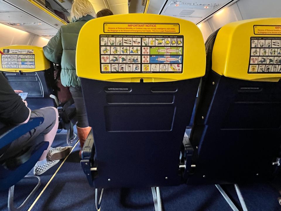The back of a seat on a Ryanair Boeing 737-800 is mostly navy but yellow at the headrest, with the safety card printed onto it.
