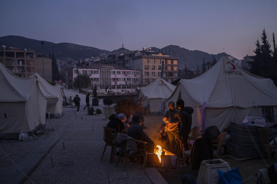 People gather around a bonfire at a temporary camp for residents who lost their homes during the earthquake in Antakya, southeastern Turkey, Monday, Feb. 13, 2023. Thousands left homeless by a massive earthquake that struck Turkey and Syria a week ago packed into crowded tents or lined up in the streets Monday for hot meals as the desperate search for survivors entered what was likely its last hours. (AP Photo/Bernat Armangue)