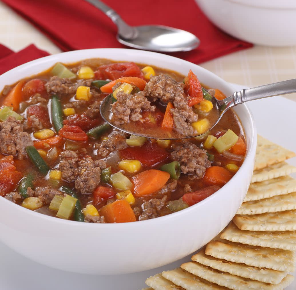 Spoonful of vegetable and beef soup above the bowl