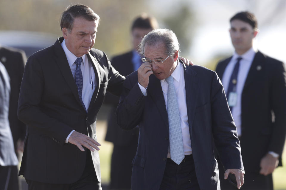 Brazil's President Jair Bolsonaro, left, talks with his Economy Minister Paulo Guedes as they arrive for the Brazilian flag-raising ceremony, in front of his official residence of the Alvorada Palace, in Brasilia, Brazil, Tuesday, Aug. 13, 2019. Brazilian students and teachers across Brazil are protesting budget cuts proposed by the Bolsonaro administration, in all major cities, including Sao Paulo, Rio de Janeiro and Brasilia. (AP Photo/Eraldo Peres)