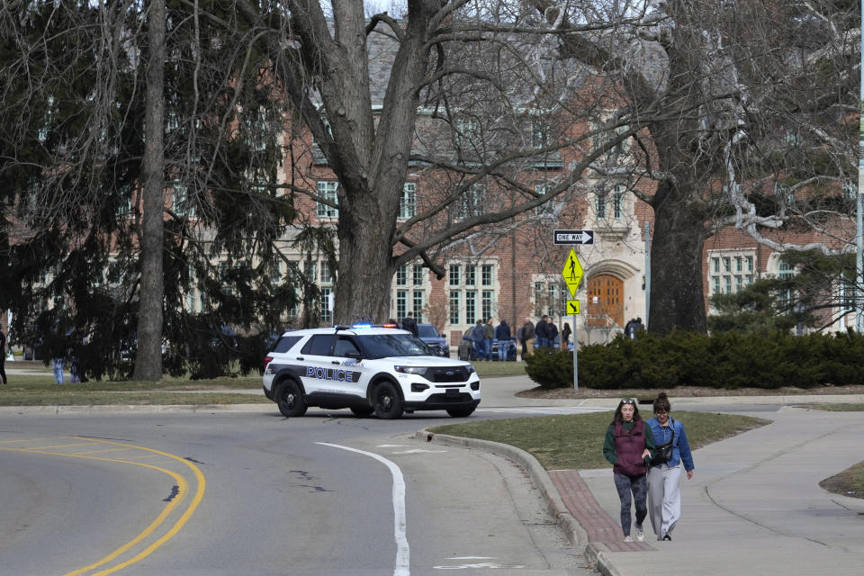 A police vehicle blocks a road as students walk on the Michigan State University campus in East Lansing, Mich., Tuesday, Feb. 14, 2023. A gunman killed several people and wounded others at Michigan State University. Police said early Tuesday that the shooter eventually killed himself. (AP Photo/Paul Sancya)