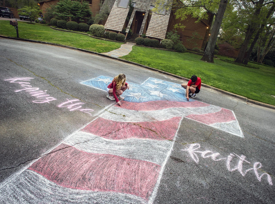 FILE - In this Monday, March 30, 2020 file photo, Layne Bjornseth, left, and her boyfriend Ben Glover touch up a street mural with chalk off Southampton Court in Decatur, Ala. Bjornseth's inspiration for the artwork is to share a message of hope and encouragement the coronavirus pandemic. (Dan Busey/The Decatur Daily via AP, File)