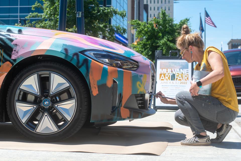 Bright vibrant colors make up the first layer while native flowers will be added as artist Jenny Meyer-McCall transforms a BMW i4 electric car into a work of art Thursday afternoon at Evergy Plaza. The car will be featured at the Mulvane Art Fair.