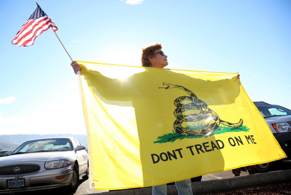 Leslie Corp holds up an American flag and the Gadsden flag while waiting outside of Roseburg Municipal Airport for President Barack Obama's arrival in Roseburg, Oregon, on Friday, Oct. 9, 2015.