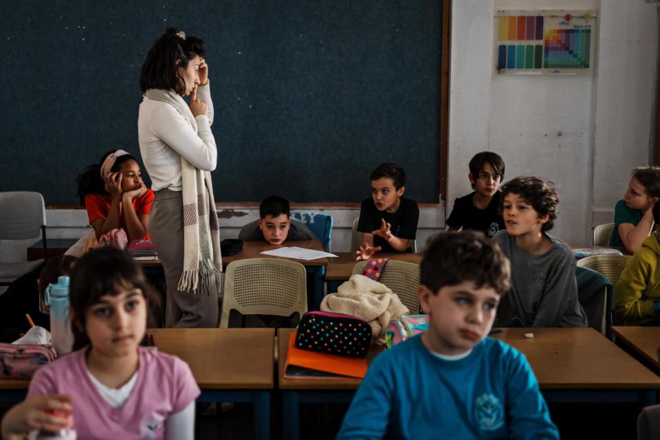 A woman stands among students seated at desks