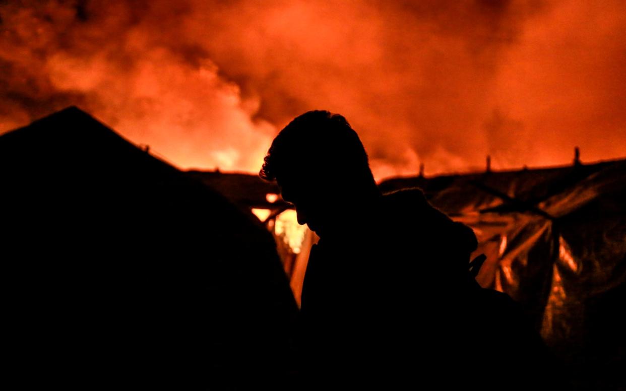 A migrant stands near tents as a fire burns in Moria camp on the island of Lesbos  - AFP