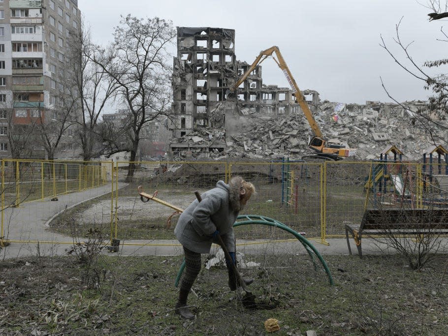 A woman digs ground as damaged buildings are being demolished by heavy duty machine as Russia-Ukraine war continues in Mariupol's Russian controlled territory, Ukraine on March 16, 2023.