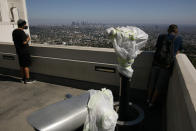 Two people stand near telescopes wrapped in plastic to prevent the spread of COVID-19 at the Griffith Observatory overlooking downtown Los Angeles, Wednesday, July 15, 2020. Coronavirus cases have surged to record levels in the Los Angeles area, putting the nation's largest county in "an alarming and dangerous phase" that if not reversed could overwhelm intensive care units and usher in more sweeping closures, health officials said Wednesday. (AP Photo/Jae C. Hong)