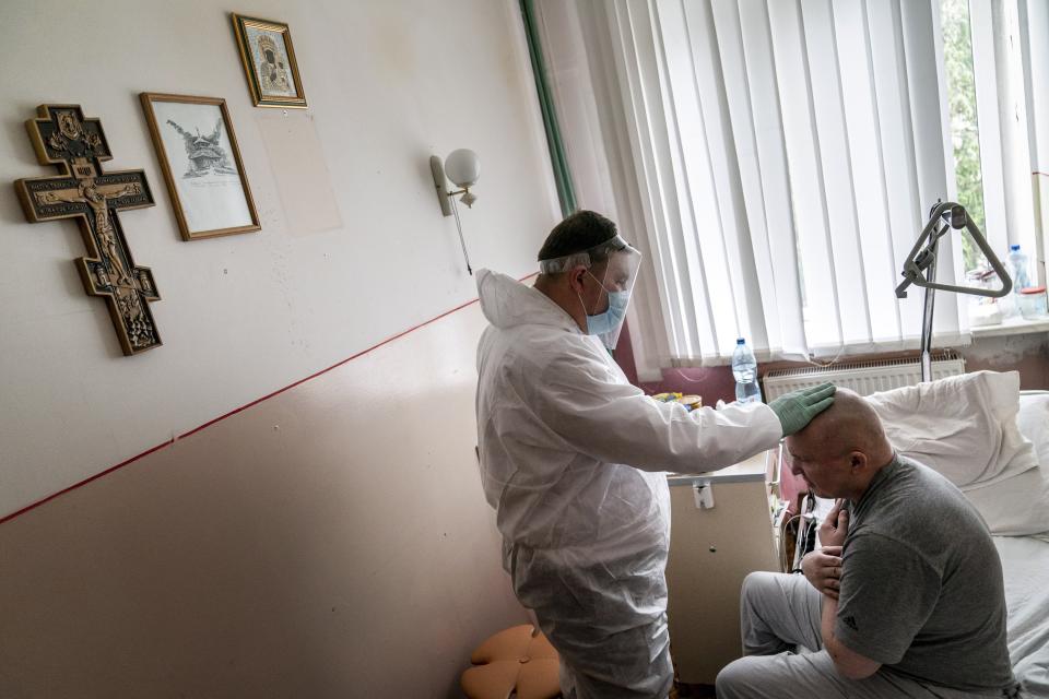 In this photo taken on Thursday, May 28, 2020, Father Yaroslav Rokhman, Ukrainian Greek Catholic Church priest, wearing protective gear to protect against coronavirus, blesses a patient at a hospice in Ivano-Frankivsk, Ukraine. Rokhman, a priest in the Ukrainian Greek Catholic Church, is pleased to be able to return to performing one of a cleric's most heartfelt duties. As the coronavirus pandemic's grip on Ukraine slowly recedes, priests received permission on May 22 to again hold services and visit the sick. (AP Photo/Evgeniy Maloletka)