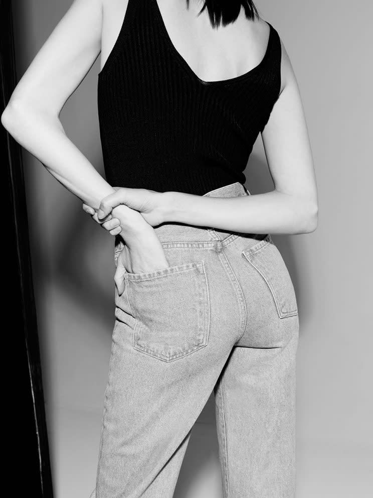 A model wears high-waisted jeans, seen from behind, hand in back pocket.