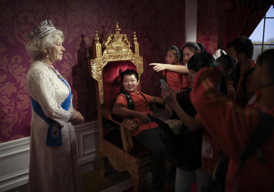 A student, center, sitting on a mock-up of the royalty chair, looks at a wax figure of Britain's Queen Elizabeth II, while others take souvenir photos, at the Madame Tussauds Museum in Beijing, China, Sept. 19, 2014. (AP Photo/Andy Wong)