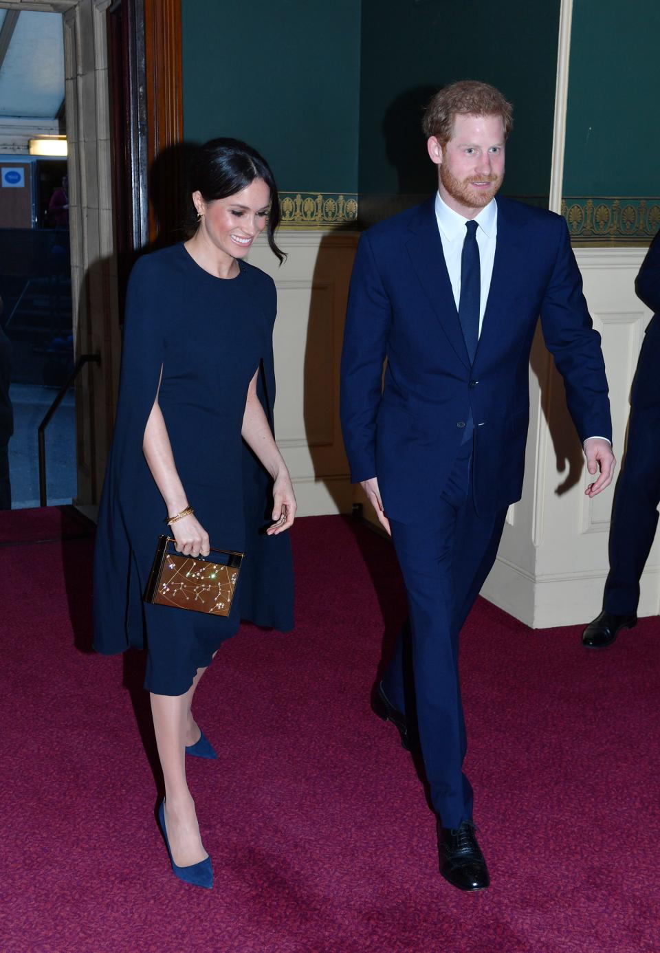 Meghan in a navy cape dress and heels and Harry in a navy suit and tie.