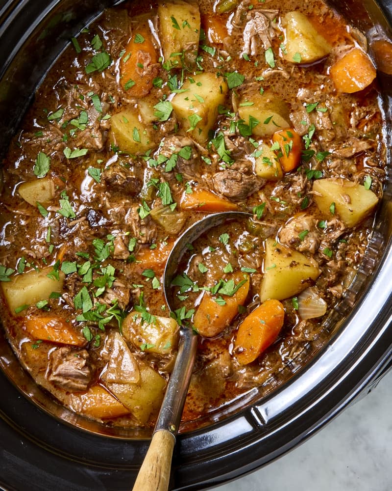 Beef stew in a slow cooker with a ladle.