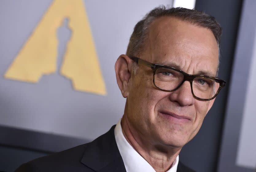 Tom Hanks poses in a black suit and glasses.