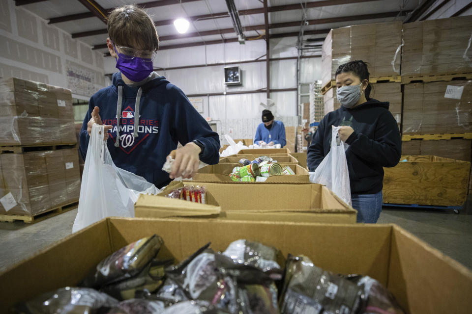 Volunteers Harris Springsteen, left, and Ana Willis, right, fill bags with food items for the backpack program at Feeding America food bank in Elizabethtown, Ky., Monday, Jan. 17, 2022. (AP Photo/Michael Clubb)