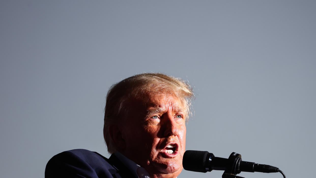 Former U.S. President Donald Trump at the microphone under a cloudless sky.