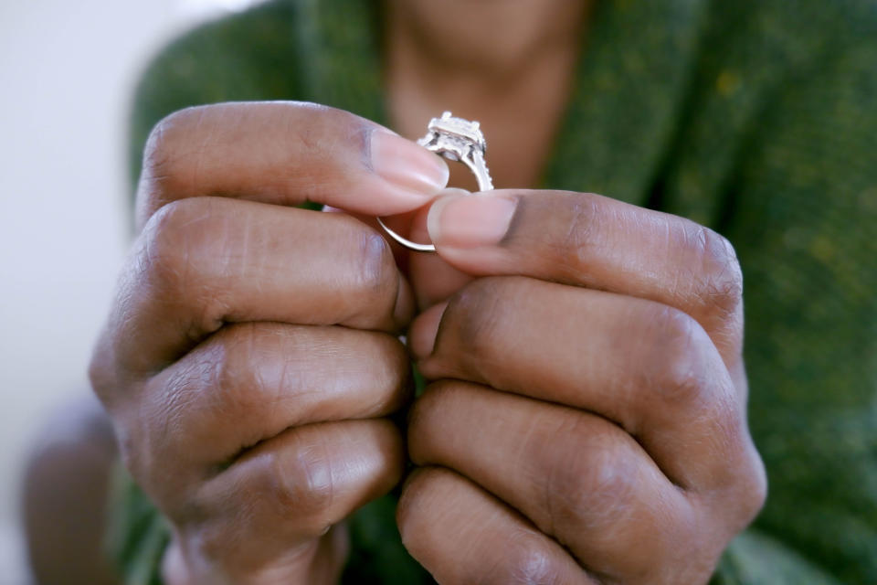 A person holds an engagement ring between their fingers, focusing on the ring's detailed design