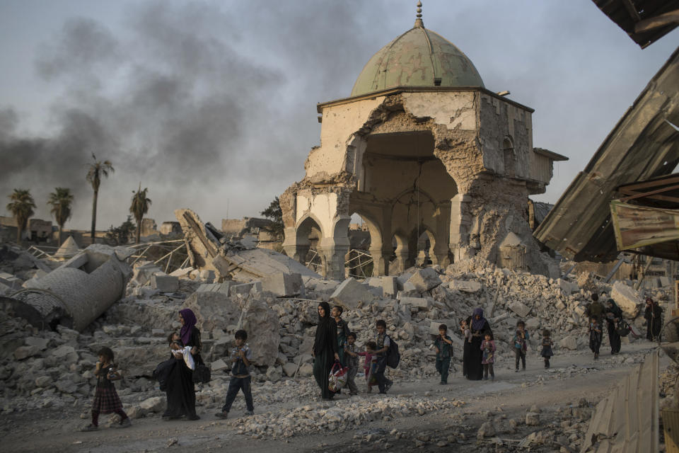 FILE - In this July 4, 2017, file photo, fleeing Iraqi civilians walk past the heavily damaged al-Nuri mosque as Iraqi forces continue their advance against Islamic State militants in Iraq's Old City of Mosul. The U.N. cultural agency has discovered five bombs hidden within the walls of the historic al-Nouri Mosque in the city of Mosul in northern Iraq, a remnant of the Islamic State militant group’s rule over the area, UNESCO said in a statement Saturday. The mosque, famous for its 12th-century leaning minaret, was destroyed by IS in 2017 and has been a focal point of UNESCO’s restoration efforts since 2020. (AP Photo/Felipe Dana, File)