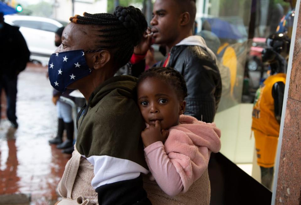 A woman wearing a face mask holds a child on her back on a crowded pavement in Pretoria  (AP)