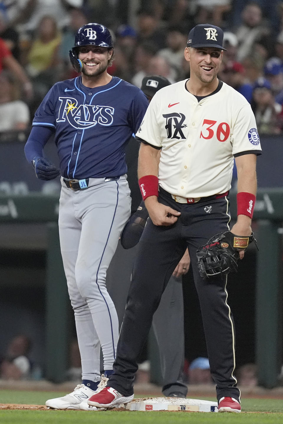 Texas Rangers first baseman Nathaniel Lowe (30) and his brother Tampa Bay Rays' Josh Lowe, left, laugh at first base after Josh singled during the sixth inning of a baseball game in Arlington, Texas, Friday, July 5, 2024. (AP Photo/LM Otero)