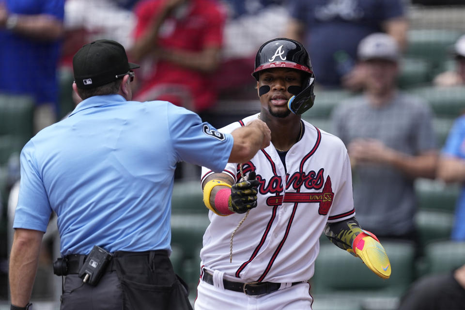 Umpire Chris Guccione (68) hands Atlanta Braves' Ronald Acuna Jr. back his gold chain after it fell off as he scored a run during the first inning of a baseball game against the Seattle Mariners, Sunday, May 21, 2023, in Atlanta. (AP Photo/John Bazemore)