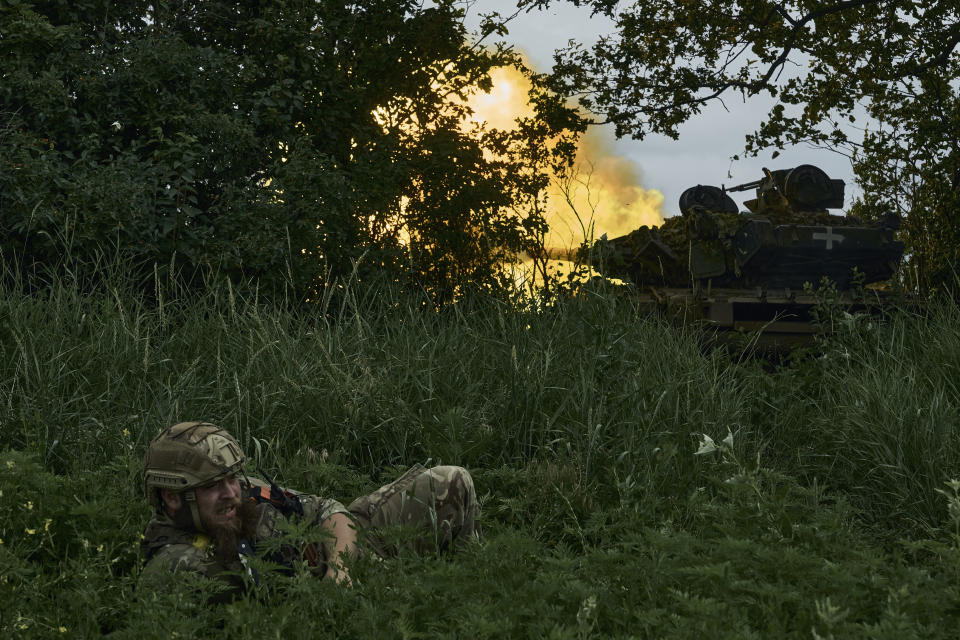 FILE - A Ukrainian soldier lies on the ground as a tank fires toward Russian positions at the frontline near Bakhmut, Donetsk region, Ukraine, Saturday, June 17, 2023. In Bakhmut, Ukrainian platoons continue to chip away at Russia’s northern and southern flanks, inching toward the strategic heights of Klischiivka. (AP Photo/Libkos, File)