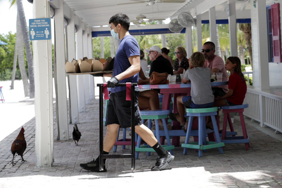 Charles Perez wears a protective face mask and gloves as he waits on tables at the Morada Bay Beach Cafe in Islamorada, in the Florida Keys, during the new coronavirus pandemic, Monday, June 1, 2020. The Florida Keys reopened for visitors Monday after the tourist-dependent island chain was closed for more than two months to prevent the spread of the coronavirus. (AP Photo/Lynne Sladky)