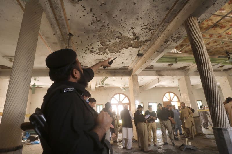 A police officer points to the damaged roof while others survey the site of a bomb blast at a religious seminary in Peshawar