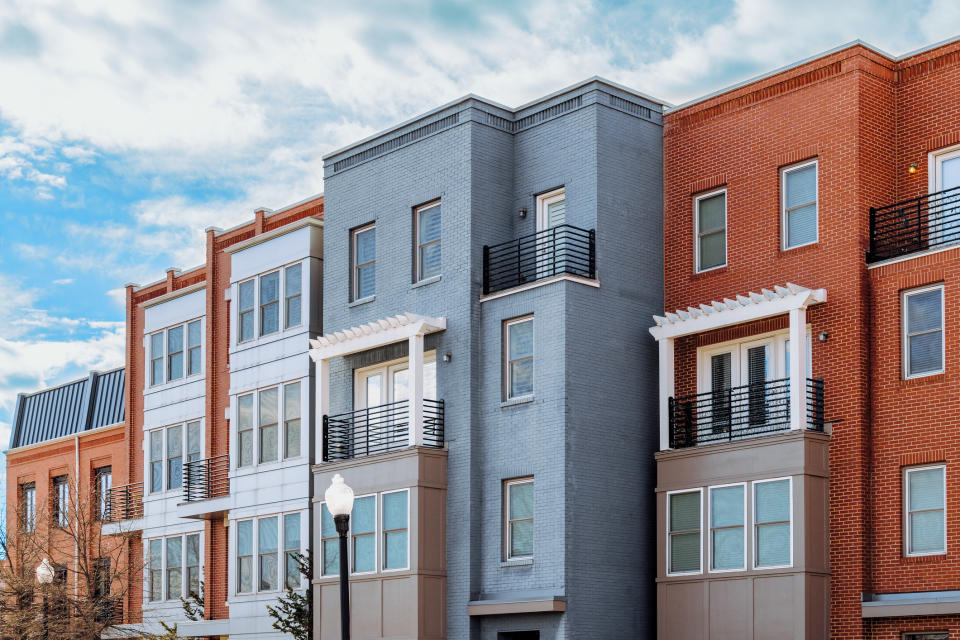 Modern row of urban townhouses featuring varied brick facades and large windows, under a partly cloudy sky