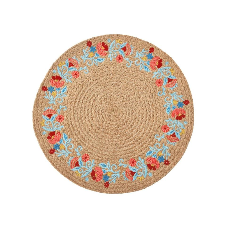 A round light brown jute placemat with light blue and red flower embroidery around the edges of it