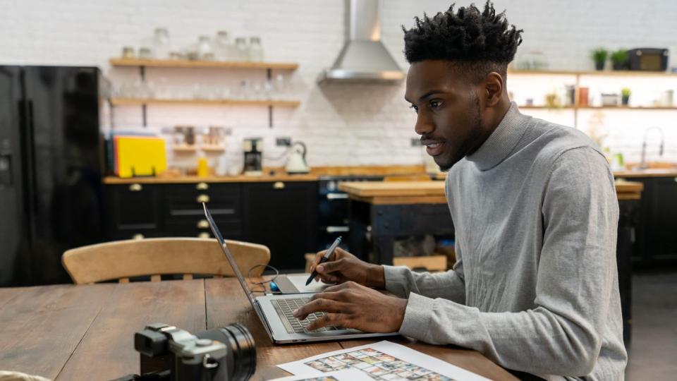 African American freelance photographer editing photos at home using a laptop computer and a pen tablet.