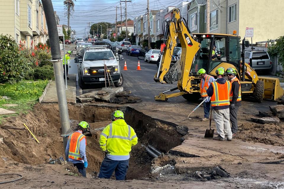 A crew repairs a large sinkhole on a street