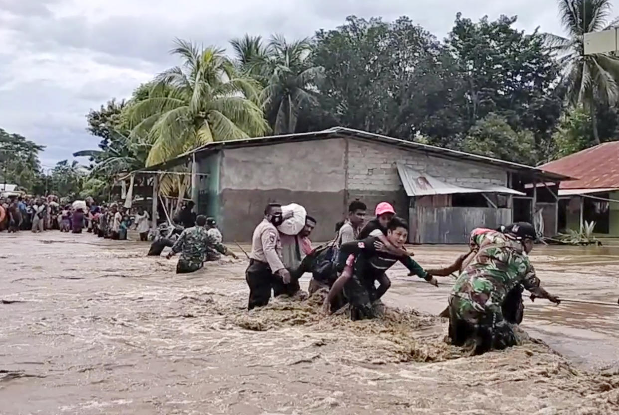 In this image made from video, soldiers and police officers assist residents to cross a flooded road in Malaka Tengah, East Nusa Tenggara province, Indonesia, Monday, April 5, 2021. Multiple disasters caused by torrential rains in eastern Indonesia have left dozens of people dead and missing and displaced thousands, the country's disaster relief agency said Monday. (AP Photo)