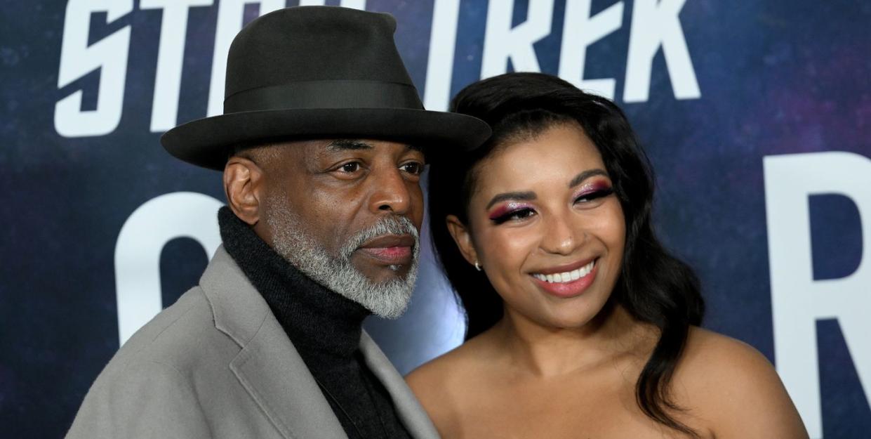 levar burton and mica burton, levar wears a black tribly hat, mica burton is smiling and wearing a strapless dress